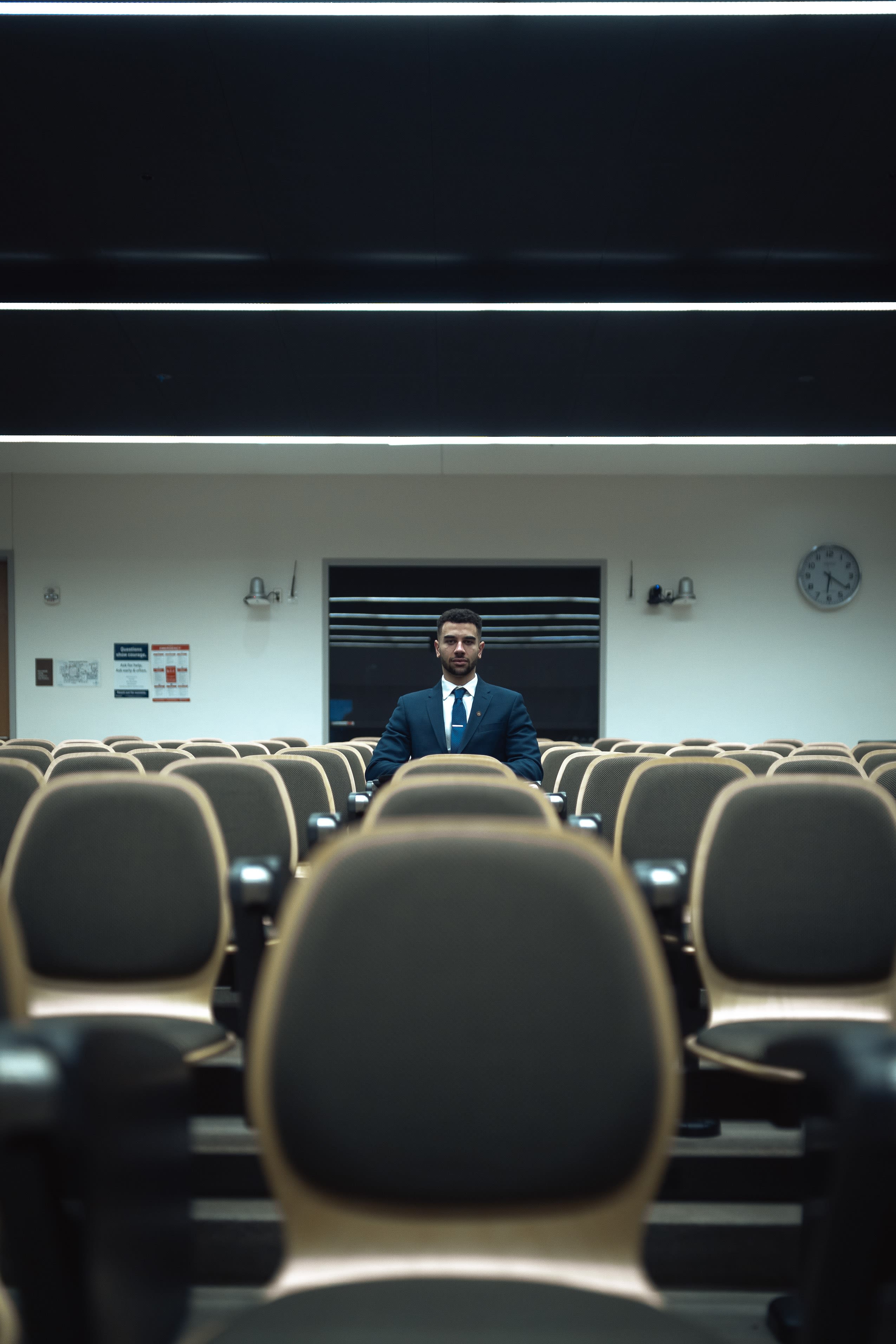 man in blue suit standing in front of brown chairs